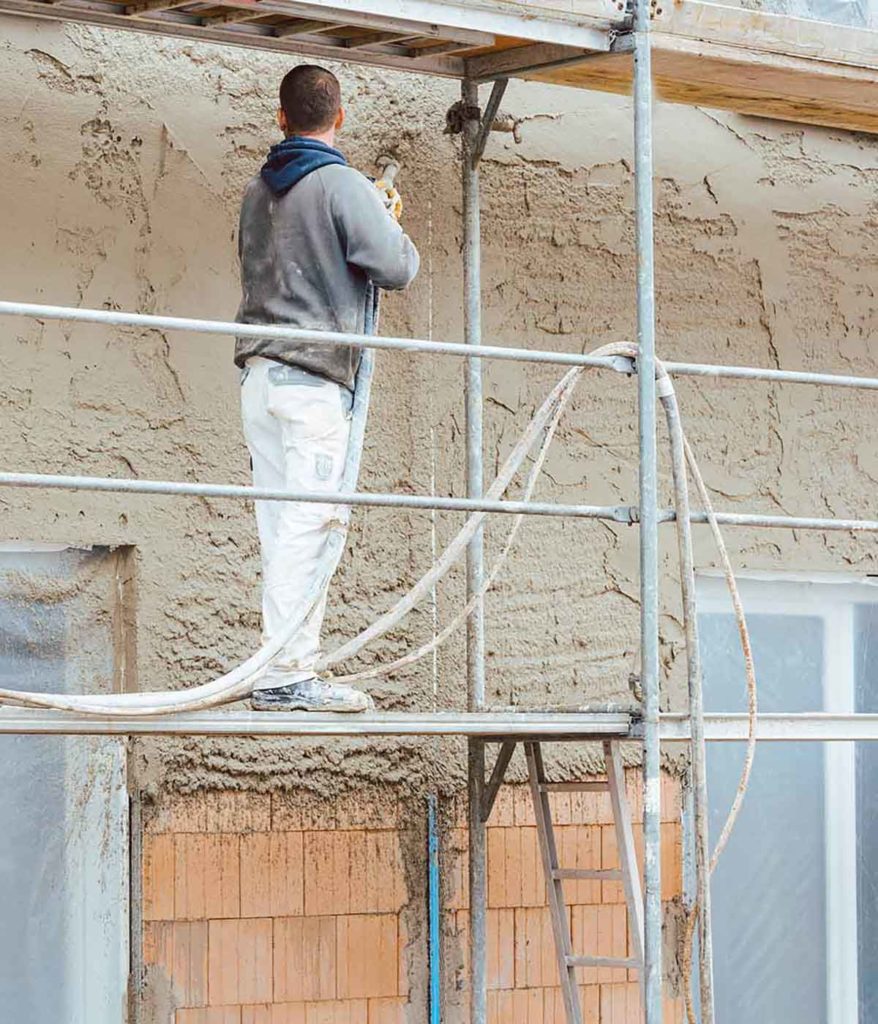 Workman standing on scaffolding spraying render mix onto the external wall of a property