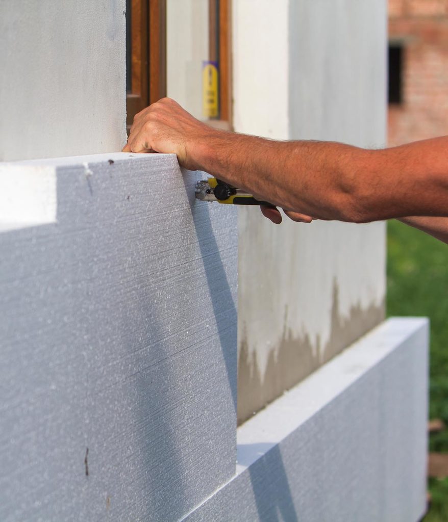 Workman trimming insulation boards as they are affixed to the external wall of a property about to be rendered.